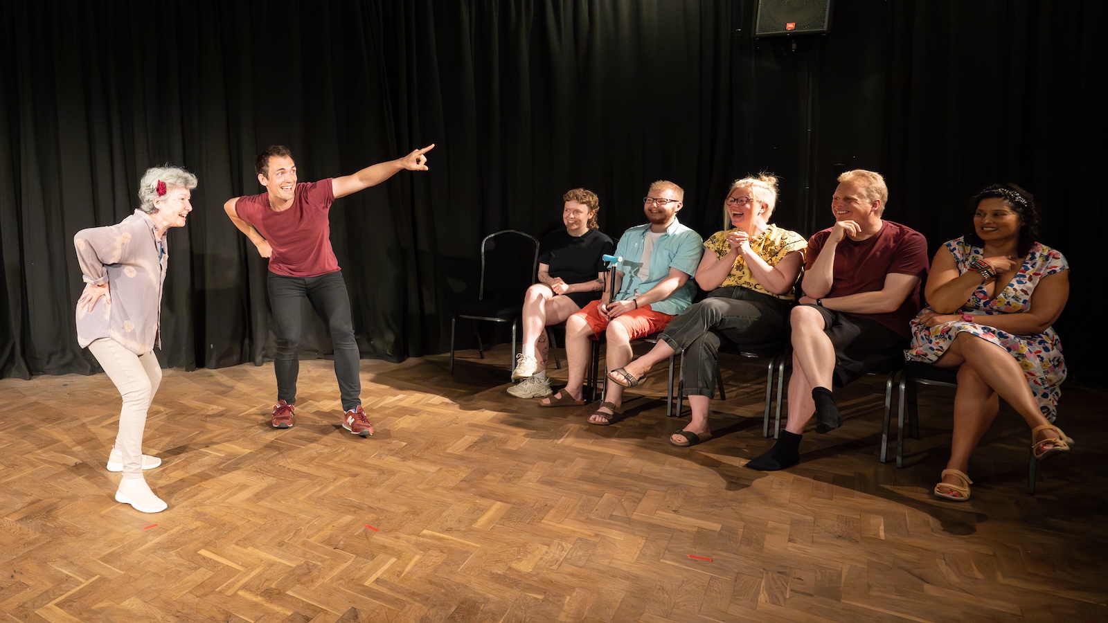 Two improv students perform a scene, watched by their classmates