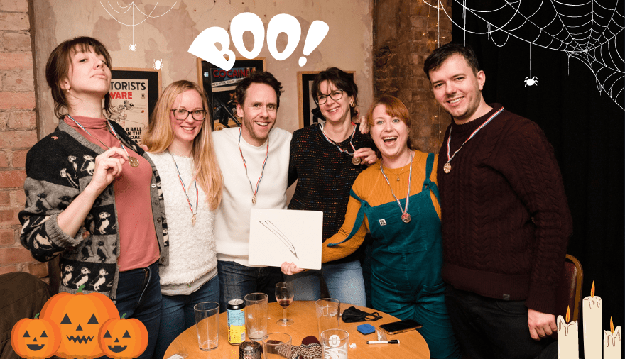 People in a bar holding up a drawing with the word "Boo" and "cobwebs" added to the image 