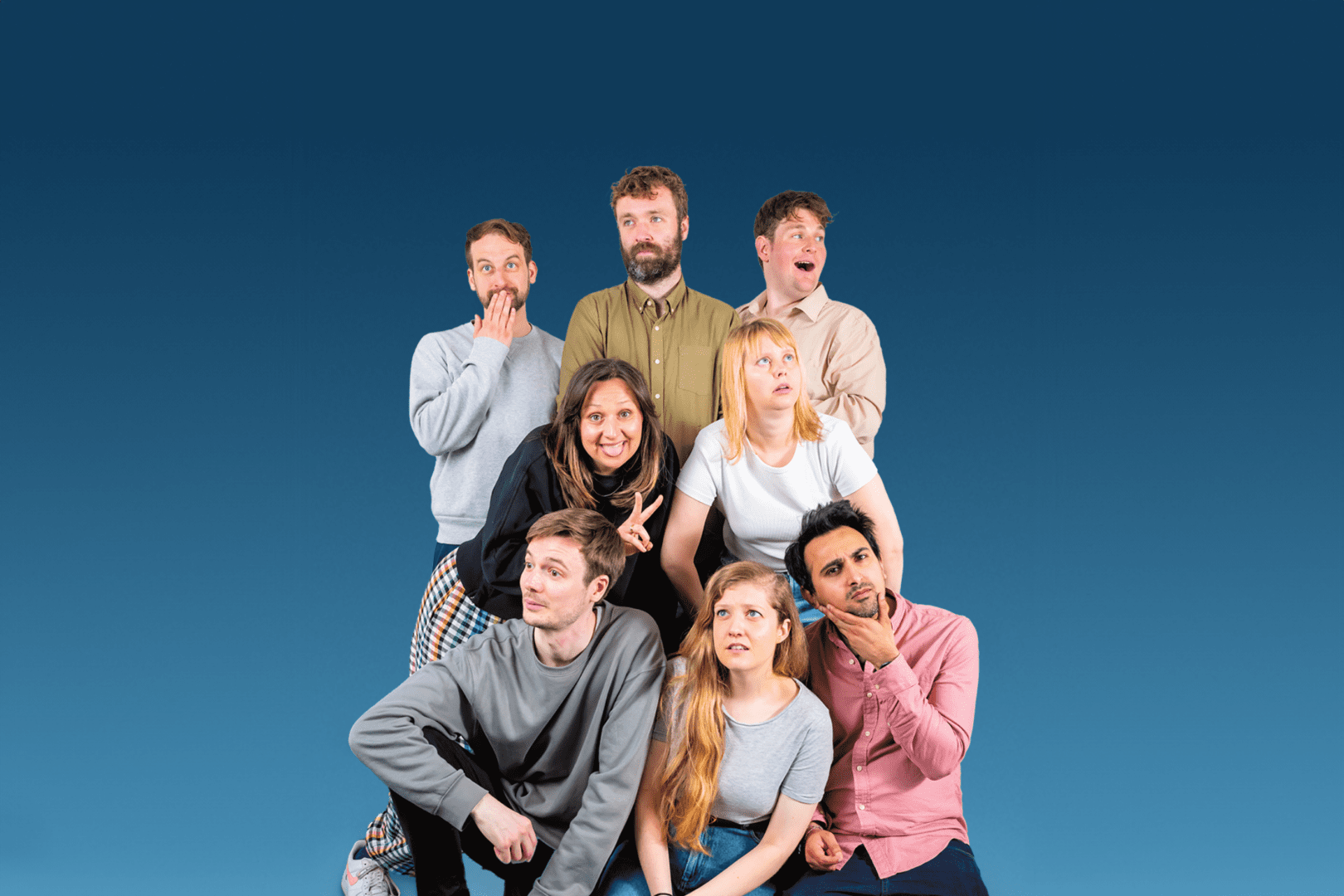 A group of 8 people are huddled at different heights doing different poses. There is a blue background.