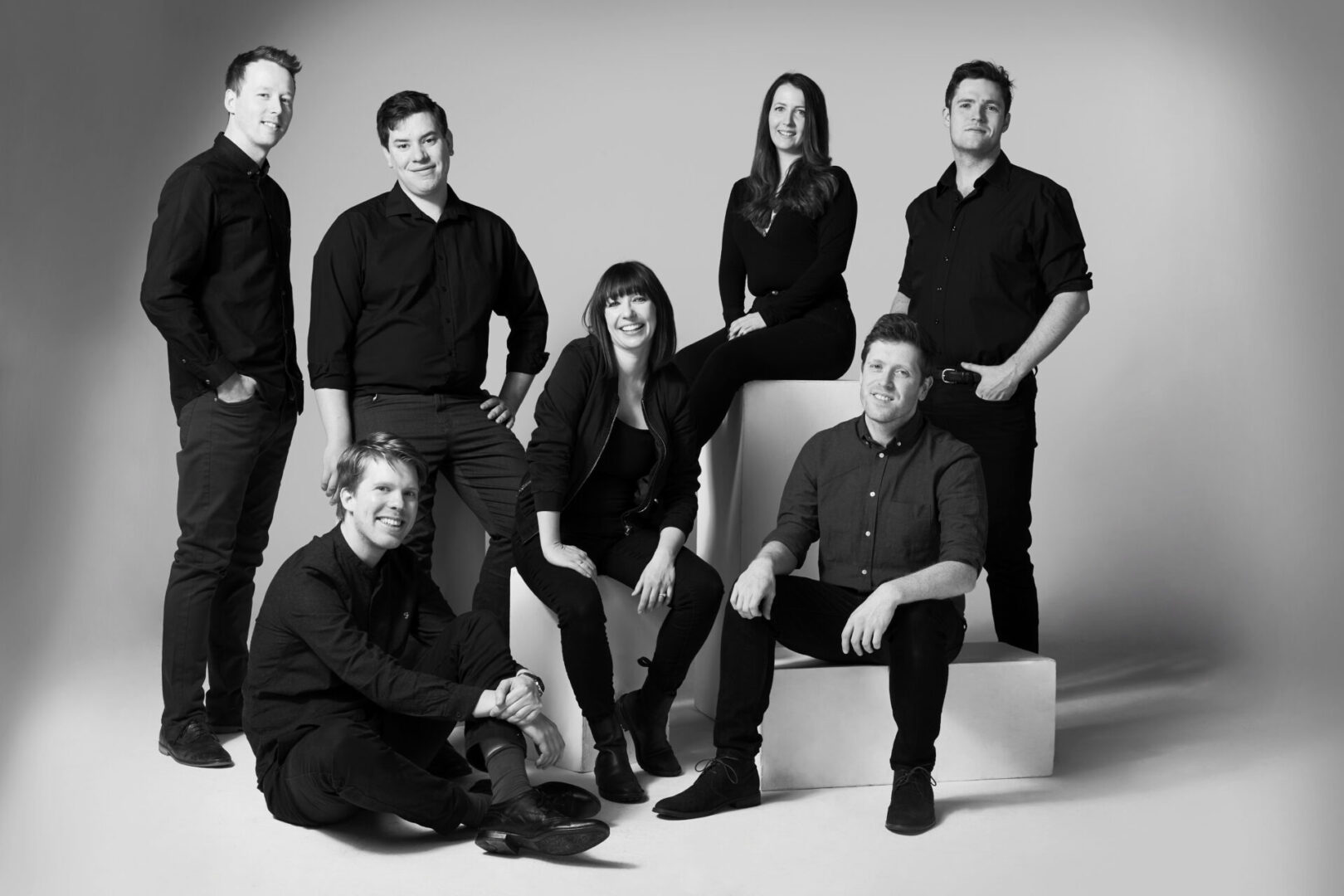 A black and white photo of 7 people stood and sat at different levels all smiling and looking at the camera.